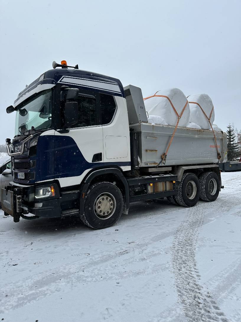 Lastebil lastet med høyballer i snøen.